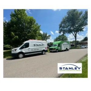 Two Stanley Heating, Cooling & Plumbing service vans are parked along a suburban street lined with trees on a sunny day, ready to assist with HVAC troubleshooting. The Stanley company logo appears in the bottom right corner of the image.