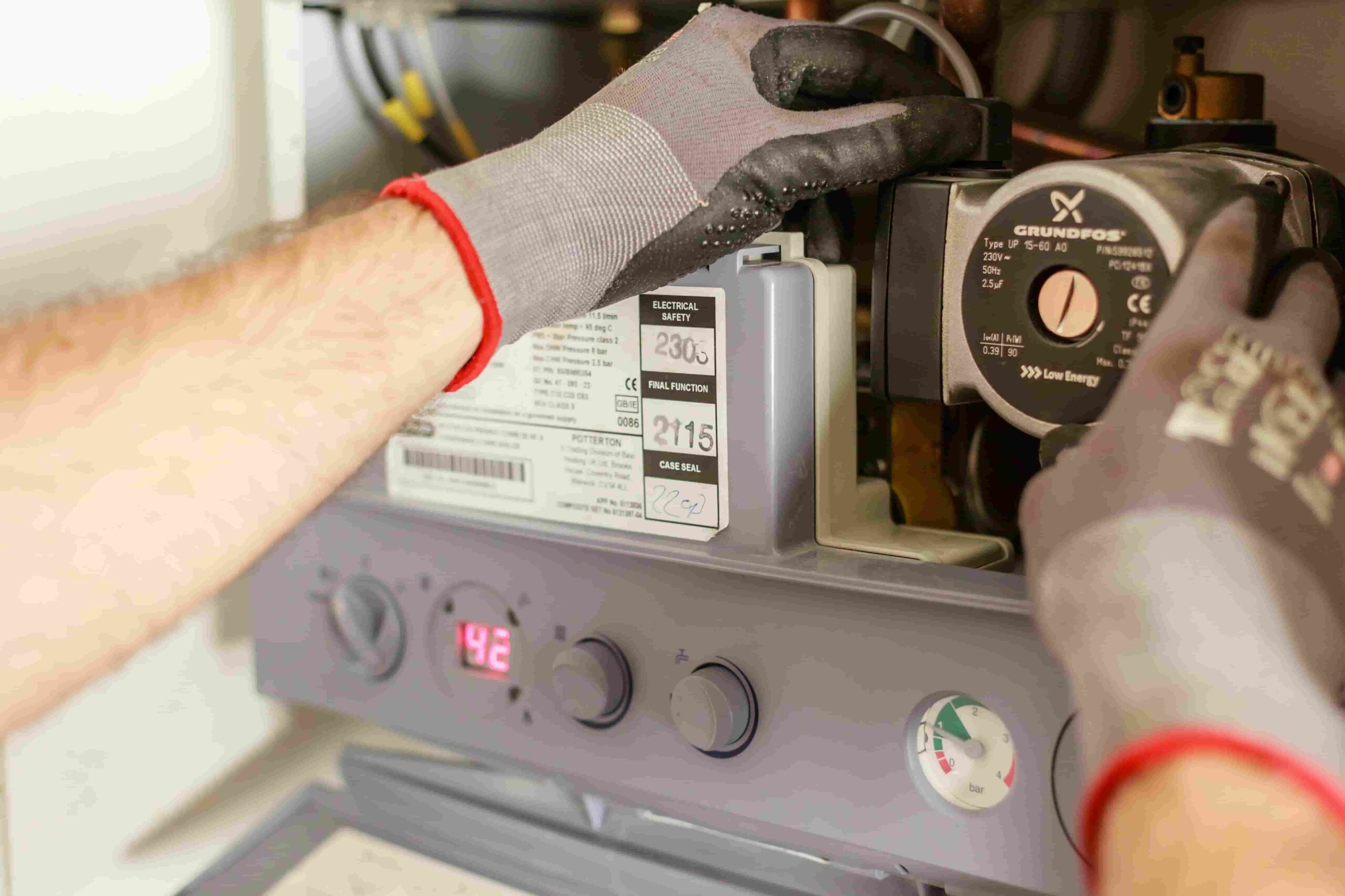 A person wearing gray gloves adjusts components inside a boiler or heating unit, with control knobs and a digital display visible on the front panel—showcasing the expertise you get when you choose best furnace repair Dayton.